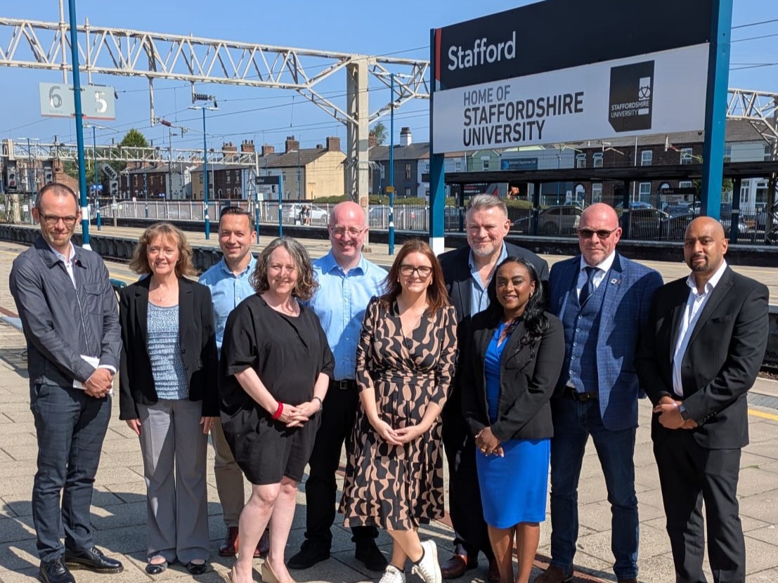 Group of people in front of sign at Stafford railway station